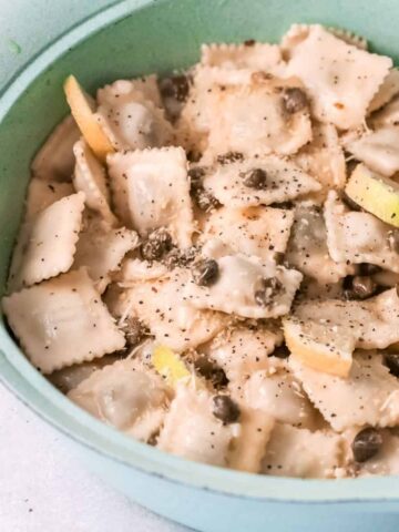 Piccata sauce with capers and lemon over ravioli in a green serving bowl.