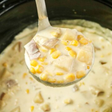 A soup ladle filled with corn chowder over a slow cooker vessel.