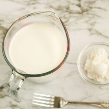 A marble counter with a clear mixing bowl filled with half and half and a fork in front of the glass.