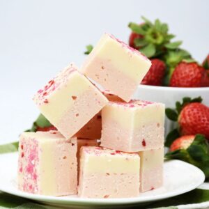 A large stack of fudge on a plate with a bowl of strawberries behind the fudge.