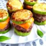 A tray of keto cheeseburger sliders on a white plate with fresh basil leaves on the plate.