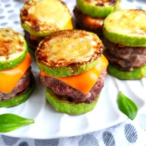 A tray of keto cheeseburger sliders on a white plate with fresh basil leaves on the plate.