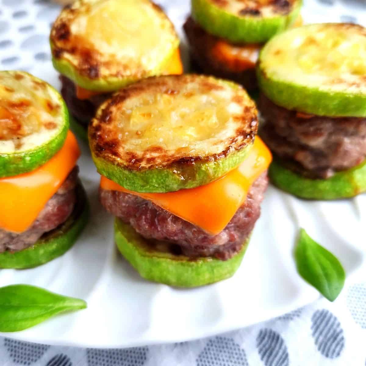 A tray of keto cheeseburger sliders on a white plate with fresh basil leaves on the plate.