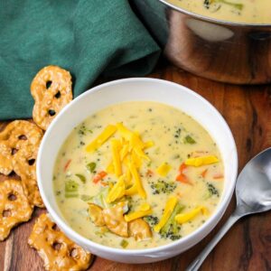 A white bowl filled with soup, broccoli, and shredded cheese with a spoon on the side.