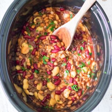 A slow cooker vessel with cooked beans, kidney beans, and cooked chopped hamburger meat.