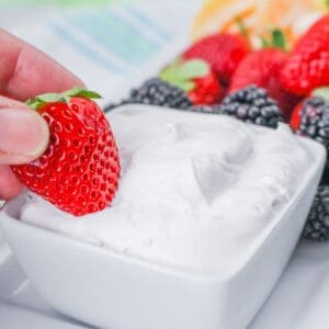 A bowl of fruit dip made with marshmallow fluff with strawberries dipped into the bowl.