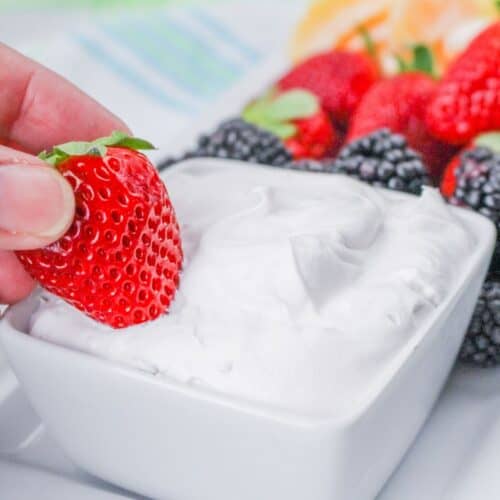 A bowl of fruit dip made with marshmallow fluff with strawberries dipped into the bowl.