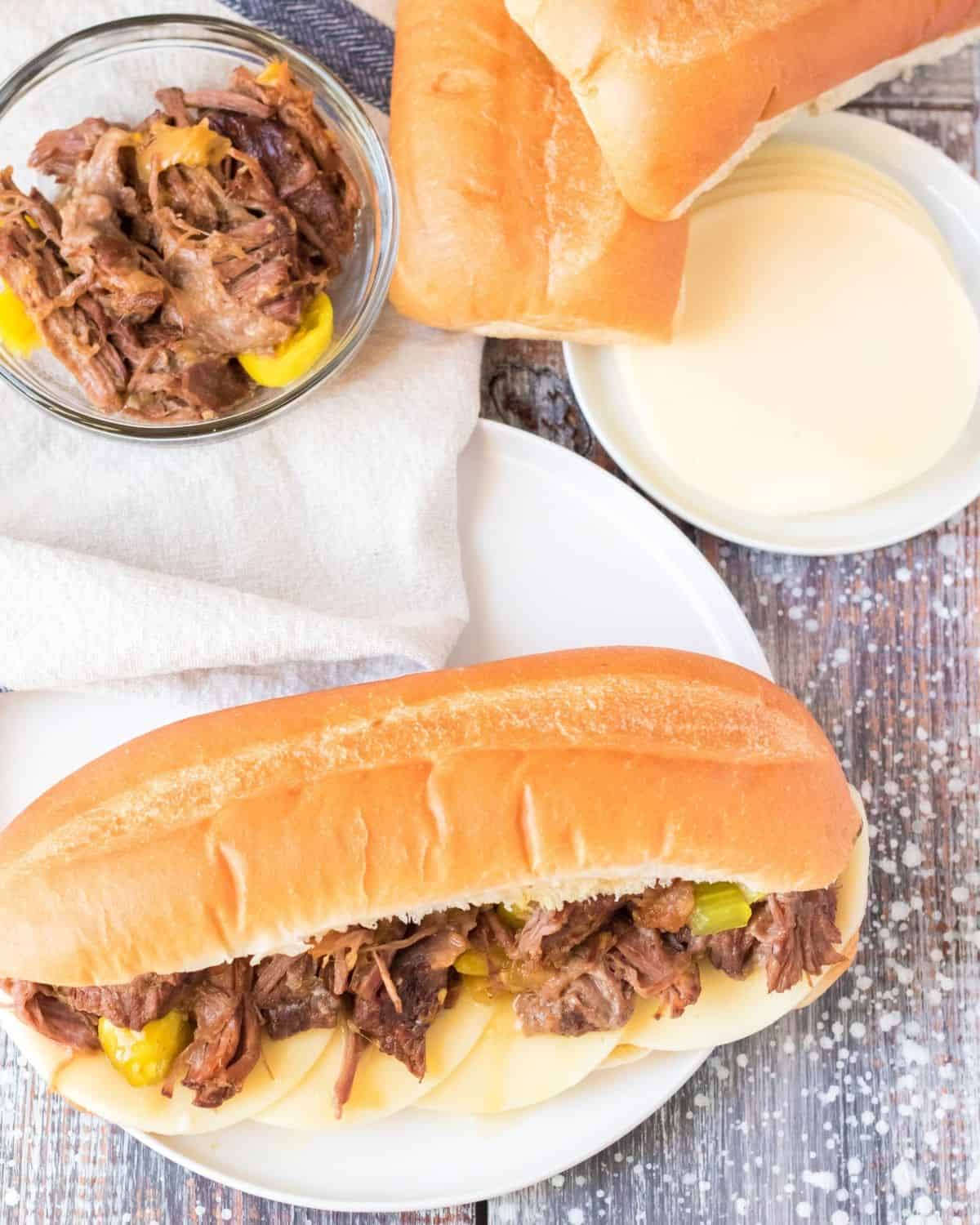 Slow Cooker Italian beef sandwiches on hoagie bread with provolone cheese and pepperocini peppers. 