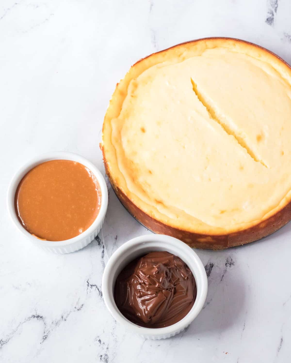 A baked cheesecake with two bowls of caramel and chocolate.