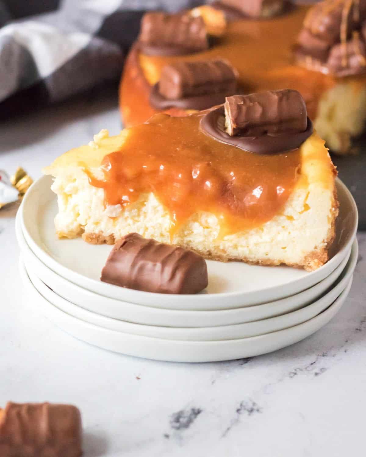 A stack of plates with a slice of twix cheesecake on th top layer with a caramel sauce and twix candy.