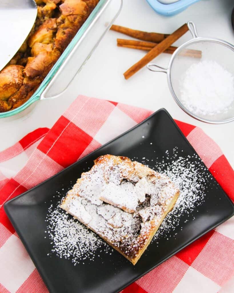 A black plate with overnight french toast casserole sprinkled with confectioners sugar. 