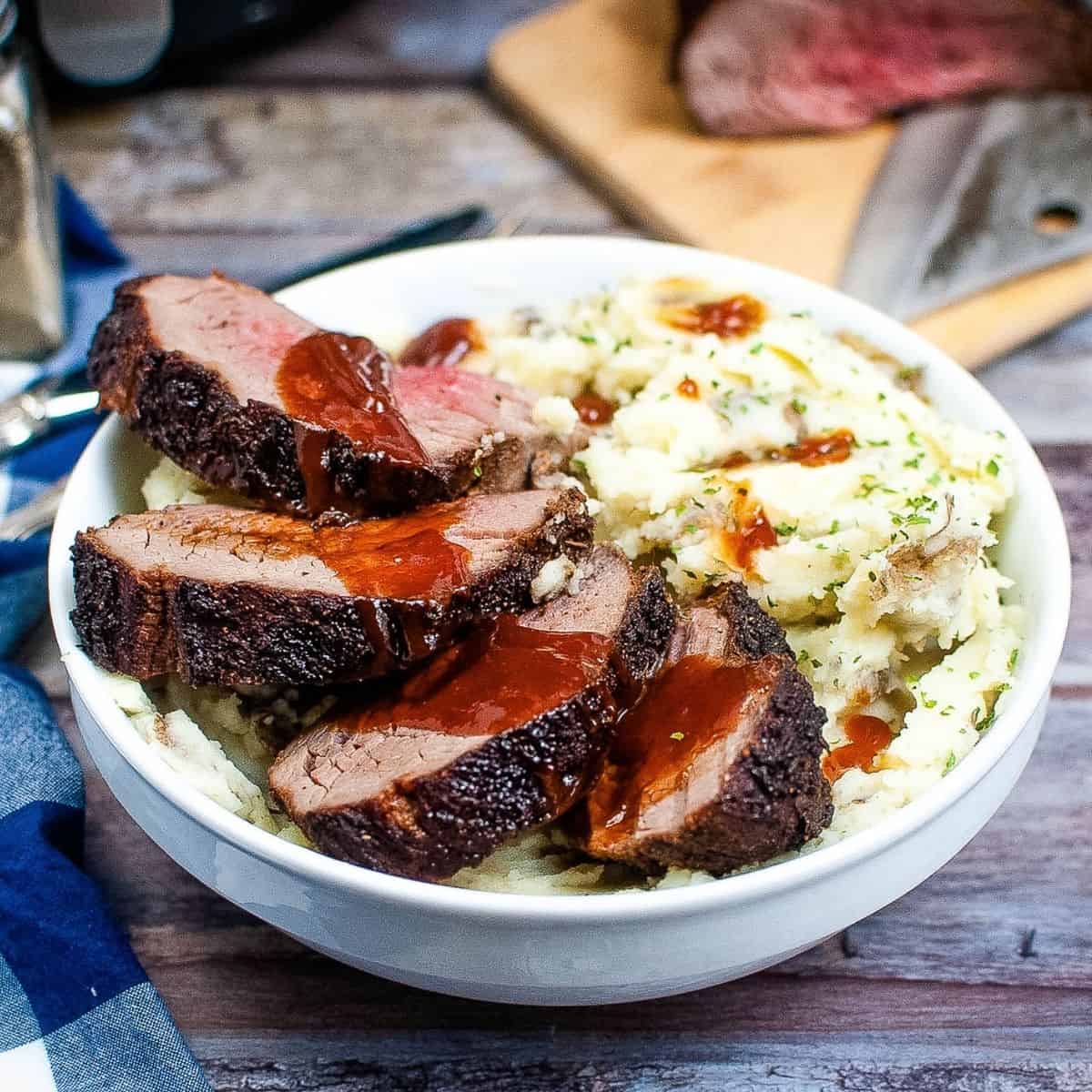 Four slices of boneless cooked steak topped with red sauce on a mashed potatoes.