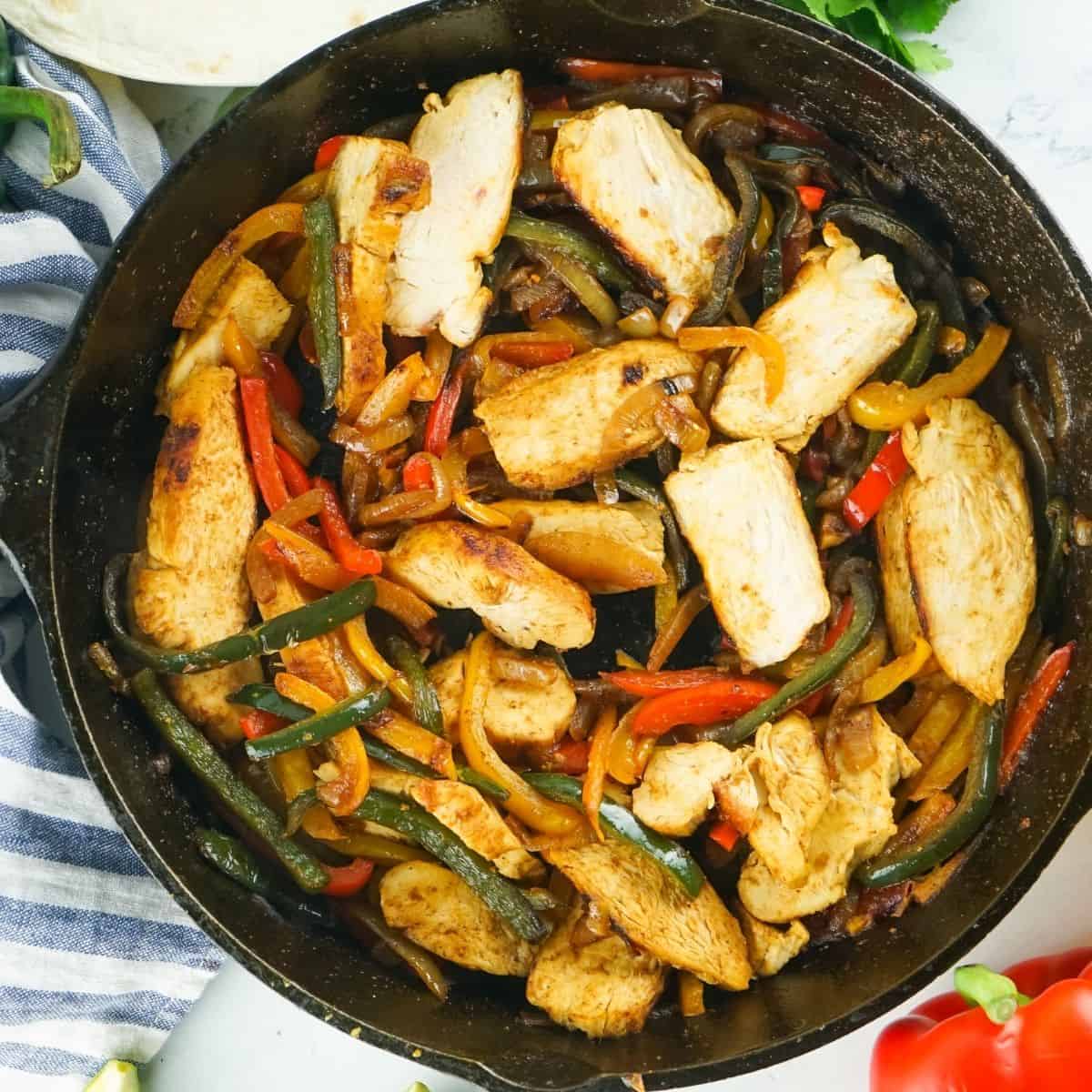 A cast iron skillet with sliced chicken, peppers, and onions.