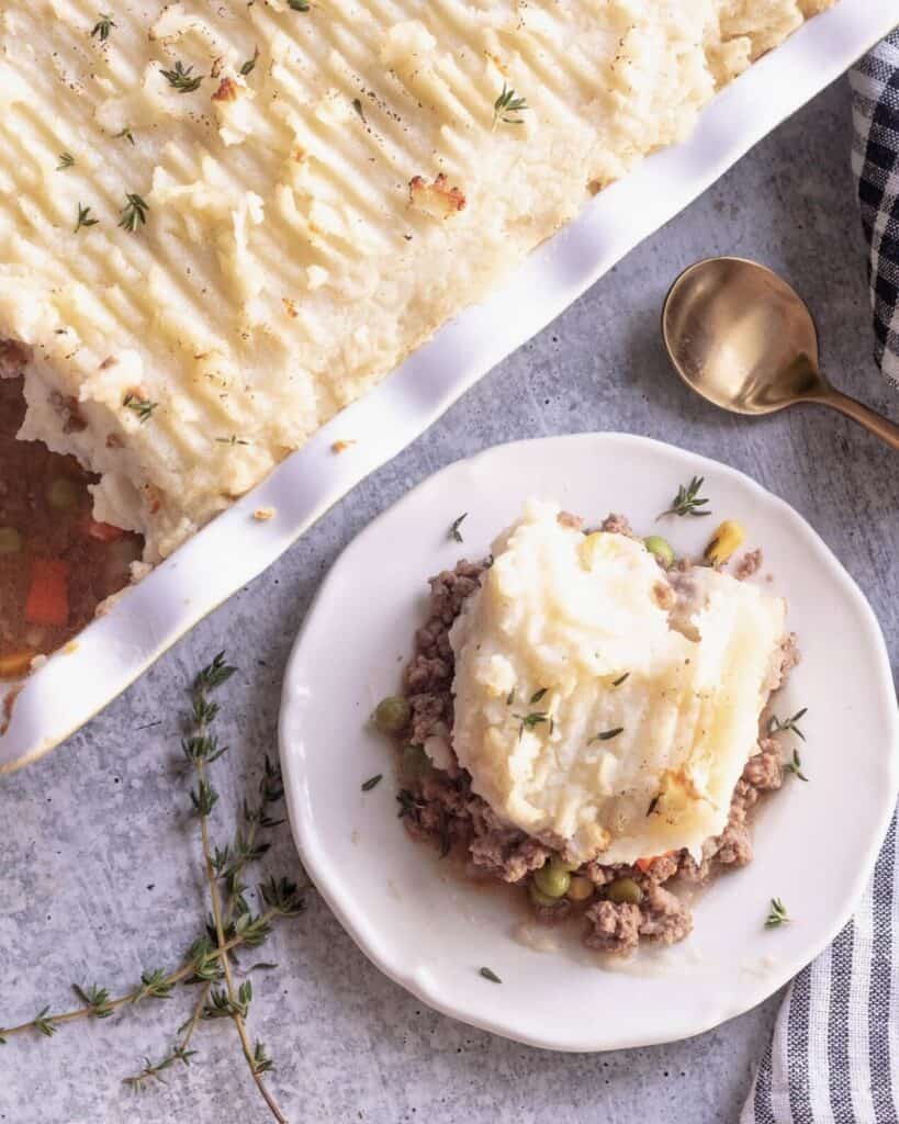 A white bowl of cottage pie next to a casserole filled with the pie filling.