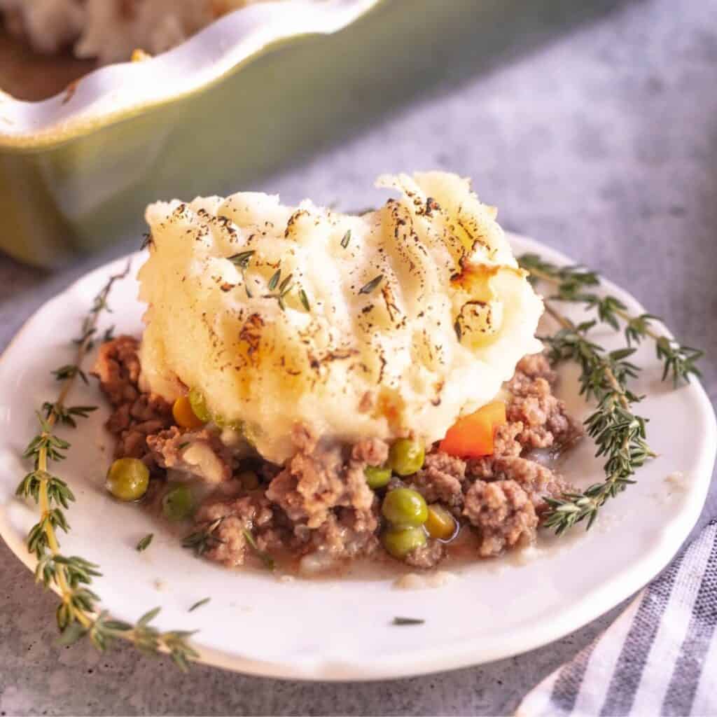 A white plate with ground beef, peas, and carrots topped with mashed potatoes.