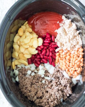 A slow cooker with ketchup, butter beans, kidney beans, pork and beans, brown sugar, and hamburger meat.