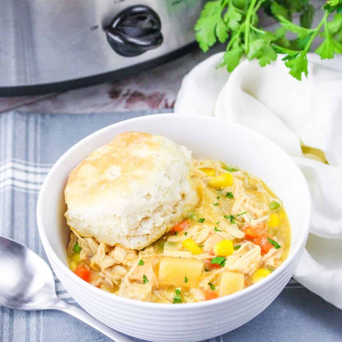 A white bowl with creamy soup, shredded chicken topped with a biscuit.