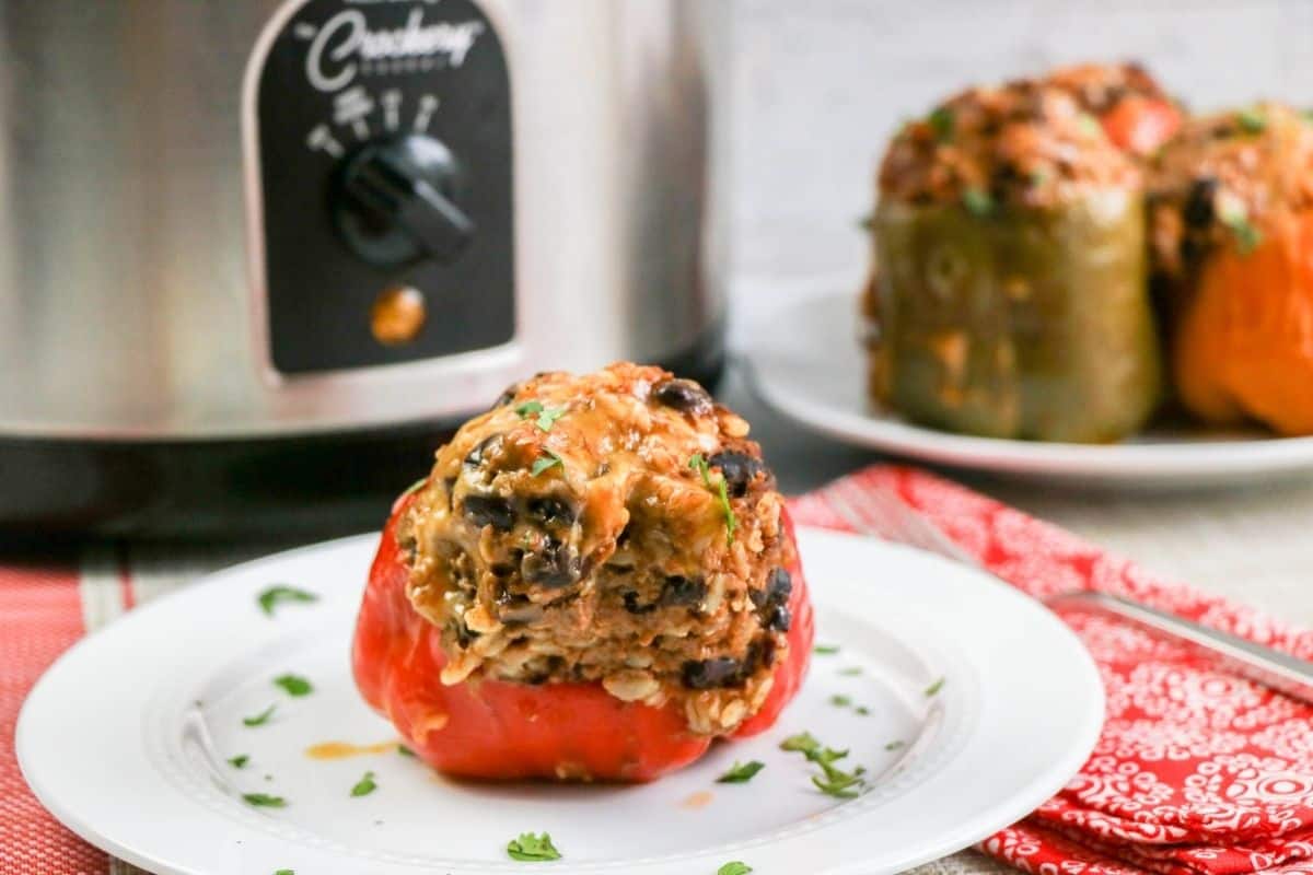 A red bell peppe stuffed with brown rice, ground beef, and beans topped with cheese. Green stuffed peppers in the background. 