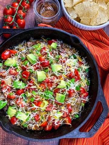 A cast iron skillet with ground beef topped with avocado, tomatoes, and cheese.