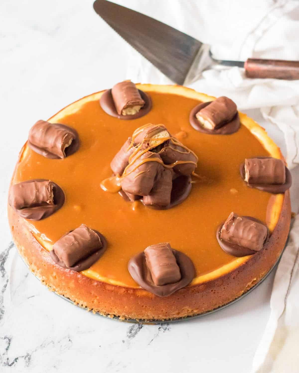 A Twix cheesecake topped with twix candy and a caramel sauce. 