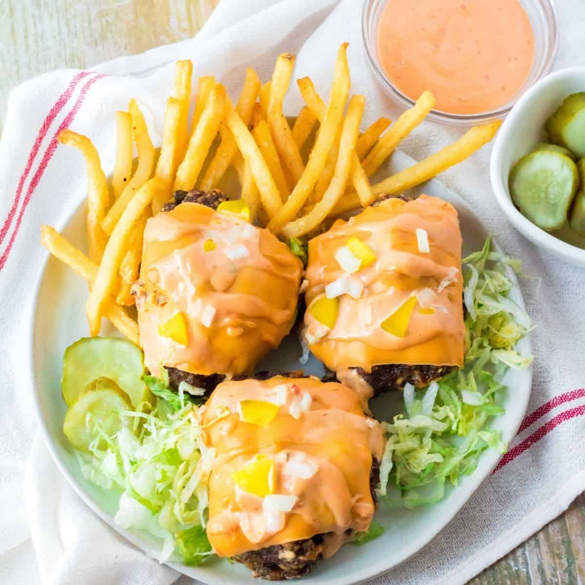 An overhead view of three mini meatloaves topped with American cheese with french fries and lettuce on a white plate.