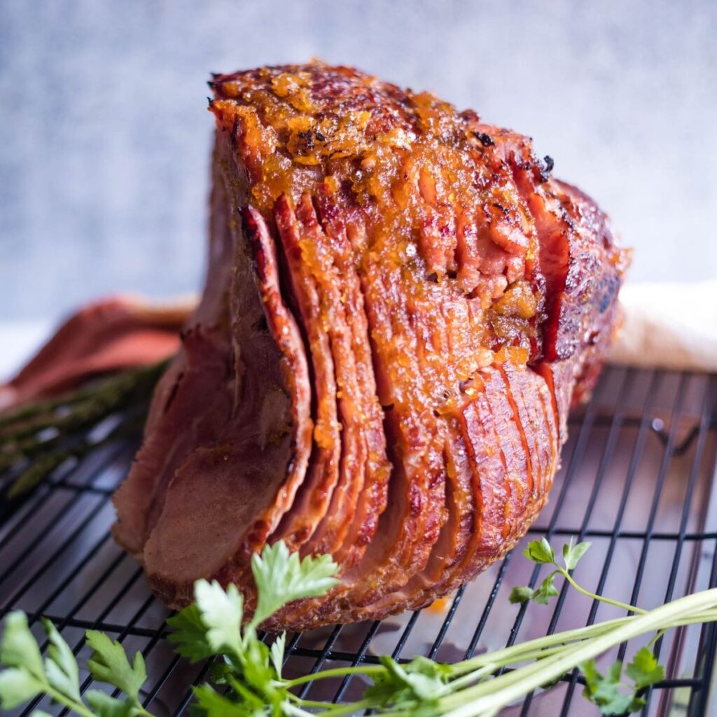 A sliced glazed ham on a baking rack with parsley on the tray.