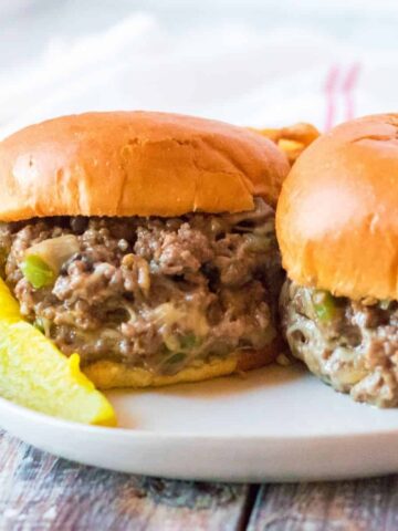 A ground beef sandwich with chopped peppers, mushrooms, and onions with cheese melted throughout on hamburger buns.