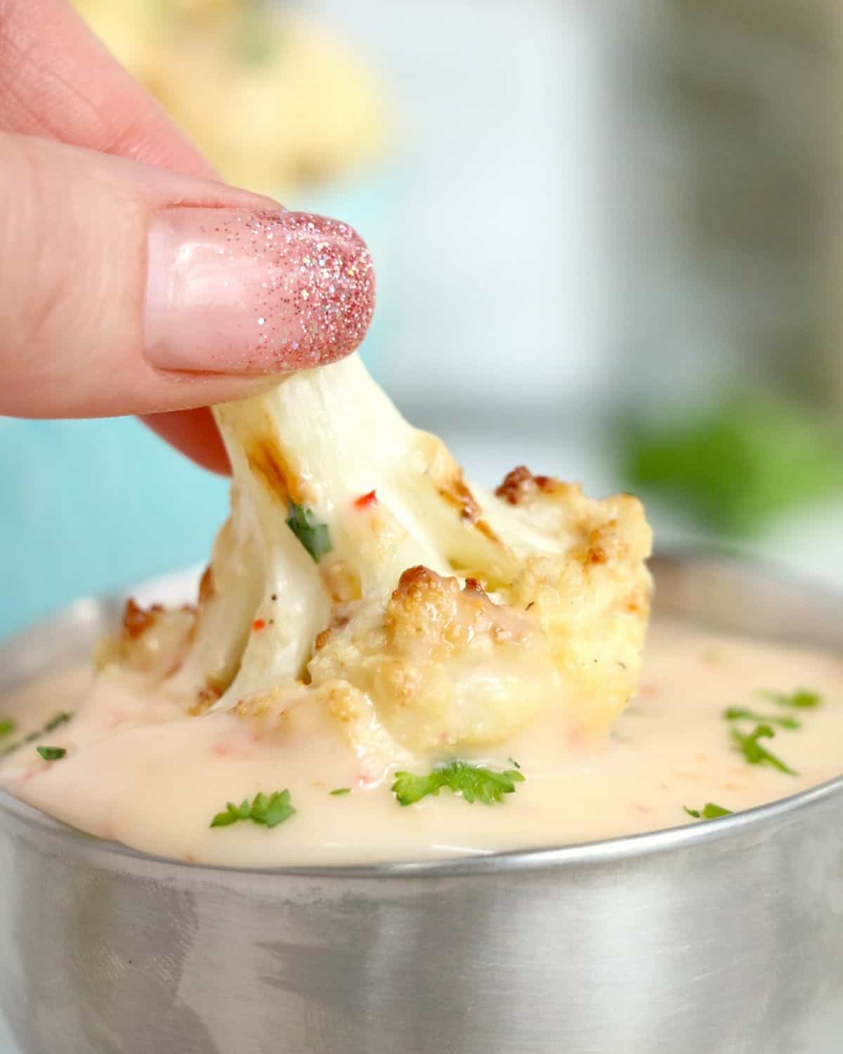 Bang bang cauliflower that has been air fried being dipped into sauce. 