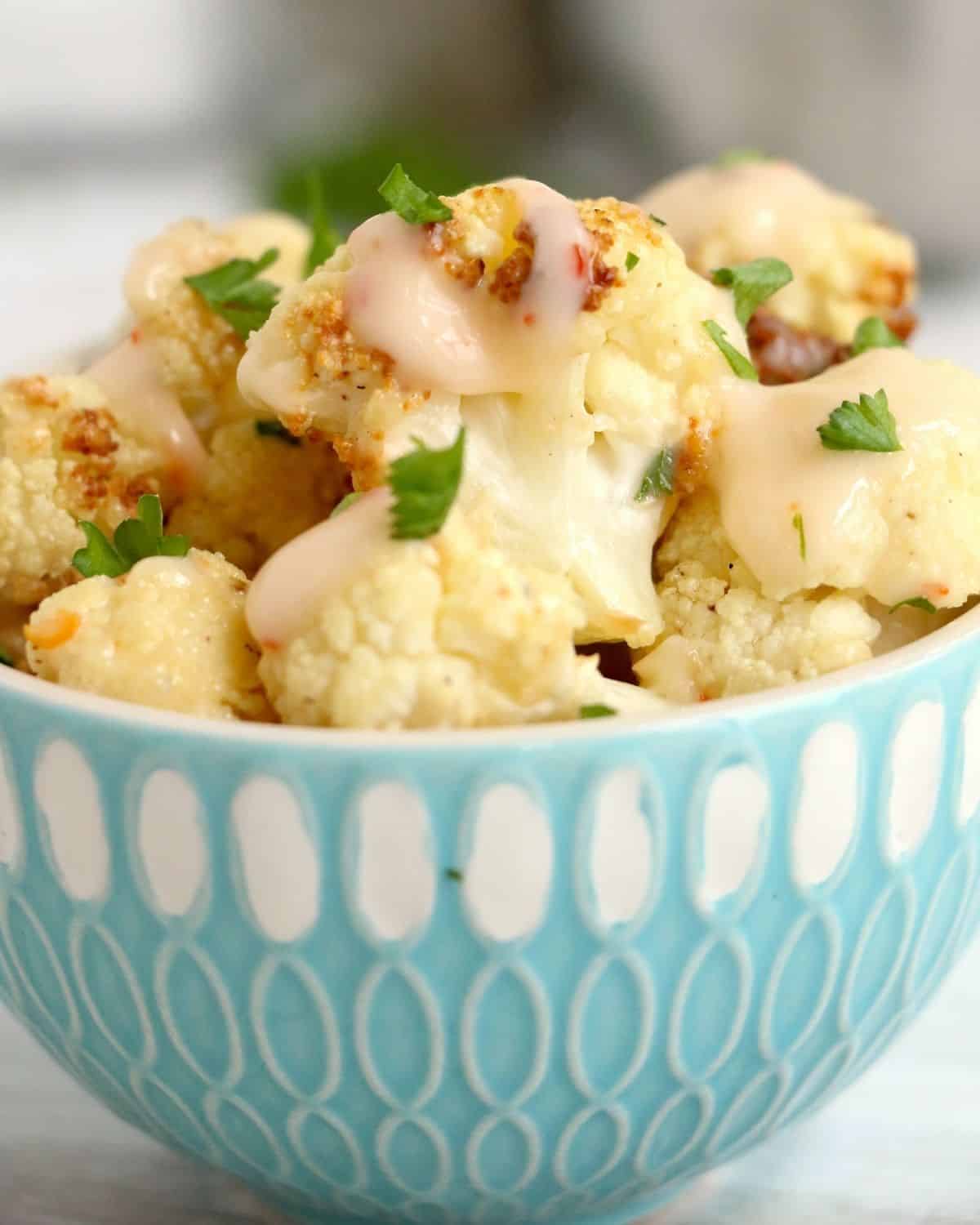 A large bowl with air fryer cauliflower topped with bang bang sauce. 