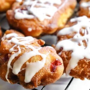 A fried apple cherry fritter with a white icing on a wire rack