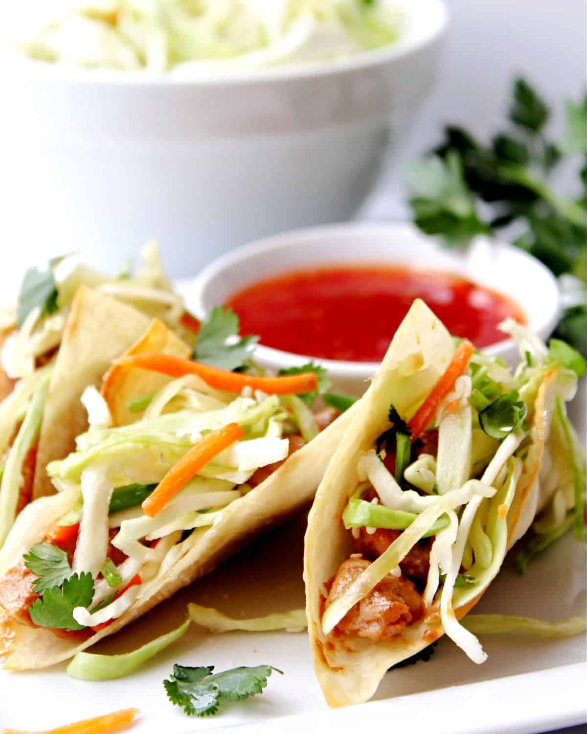 Chicken wonton tacos on a plate topped with an Asian slaw. 