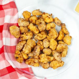 A glass plate with a red and white checkered napkin beneath it and chicken nuggets on the plate.