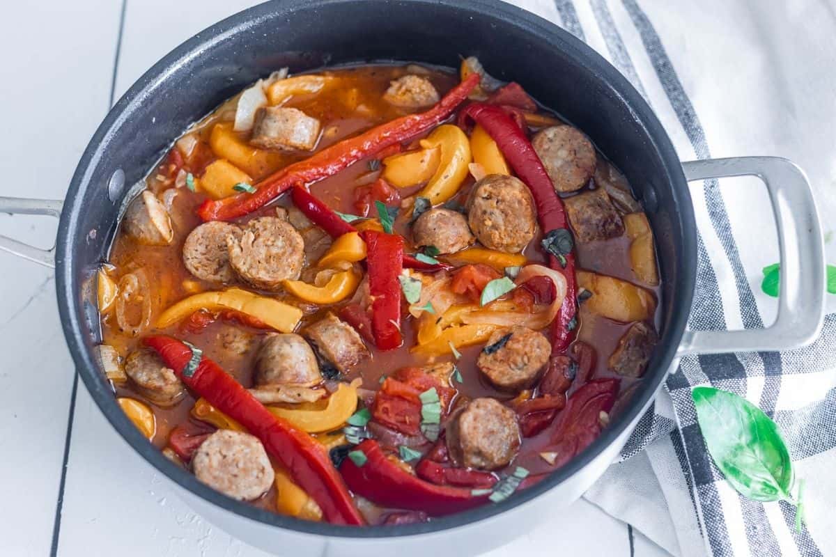 A saute pan with Italian sausages, bell  peppers and onions in sauce. 