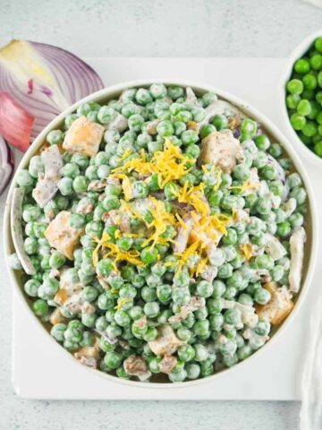 An overhead view of a white bowl filled with pea salad and bacon in a creamy white dressing topped with lemon zest.