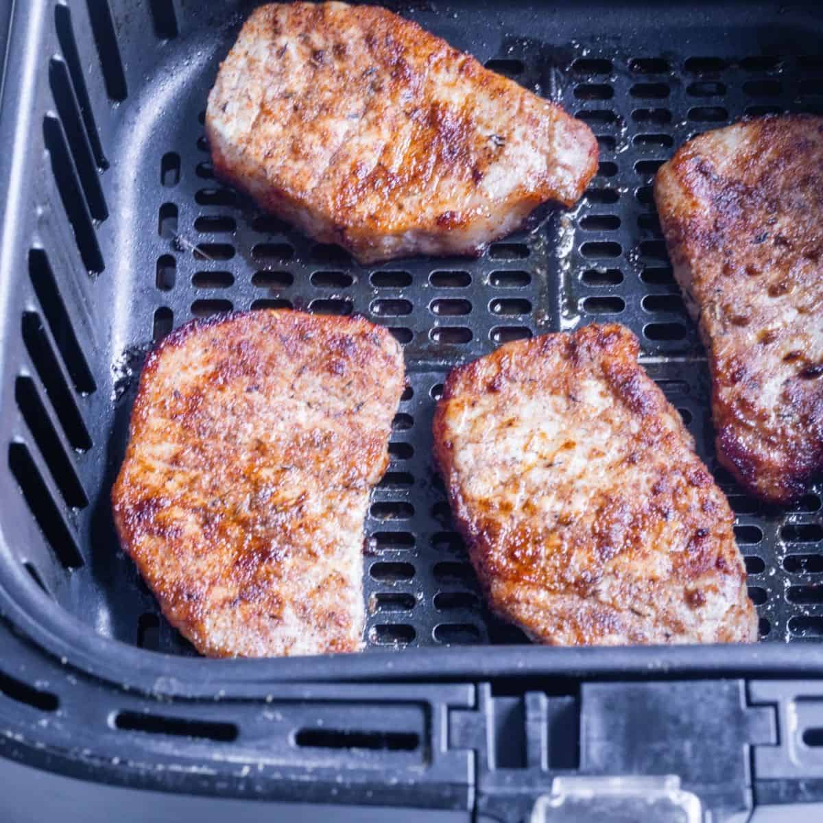 Air fryer basket with pork chops in a dry rub. 