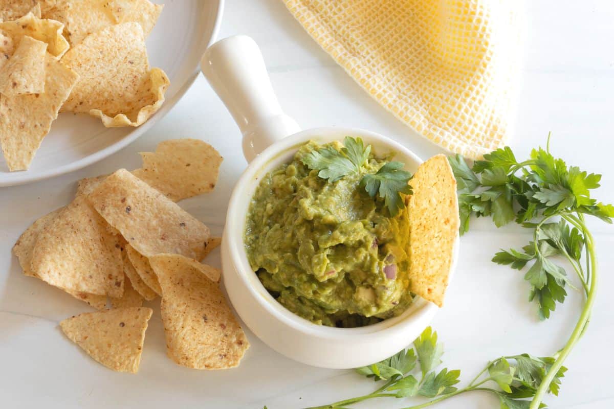 A bowl of guacamole with a tortilla chip in it and chips spread around the bowl.