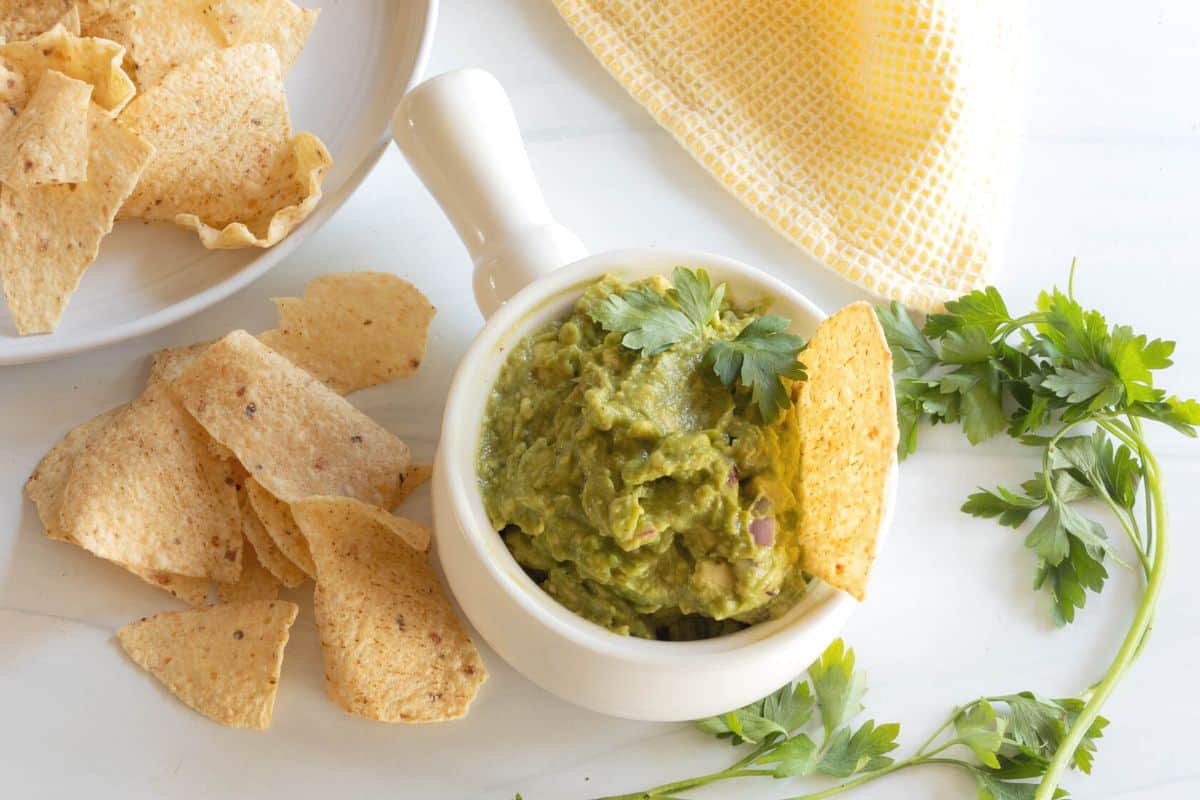 A bowl of homemade guacamole with a tortilla chip in it and chips spread around the bowl.