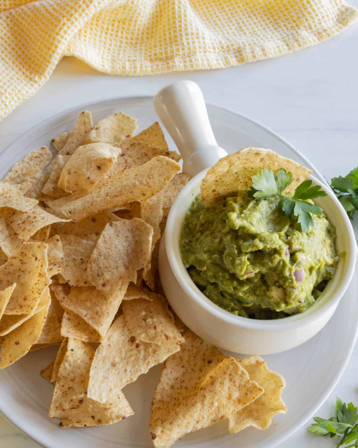 A white bowl filled with chips and a white crock with guacamole in it.