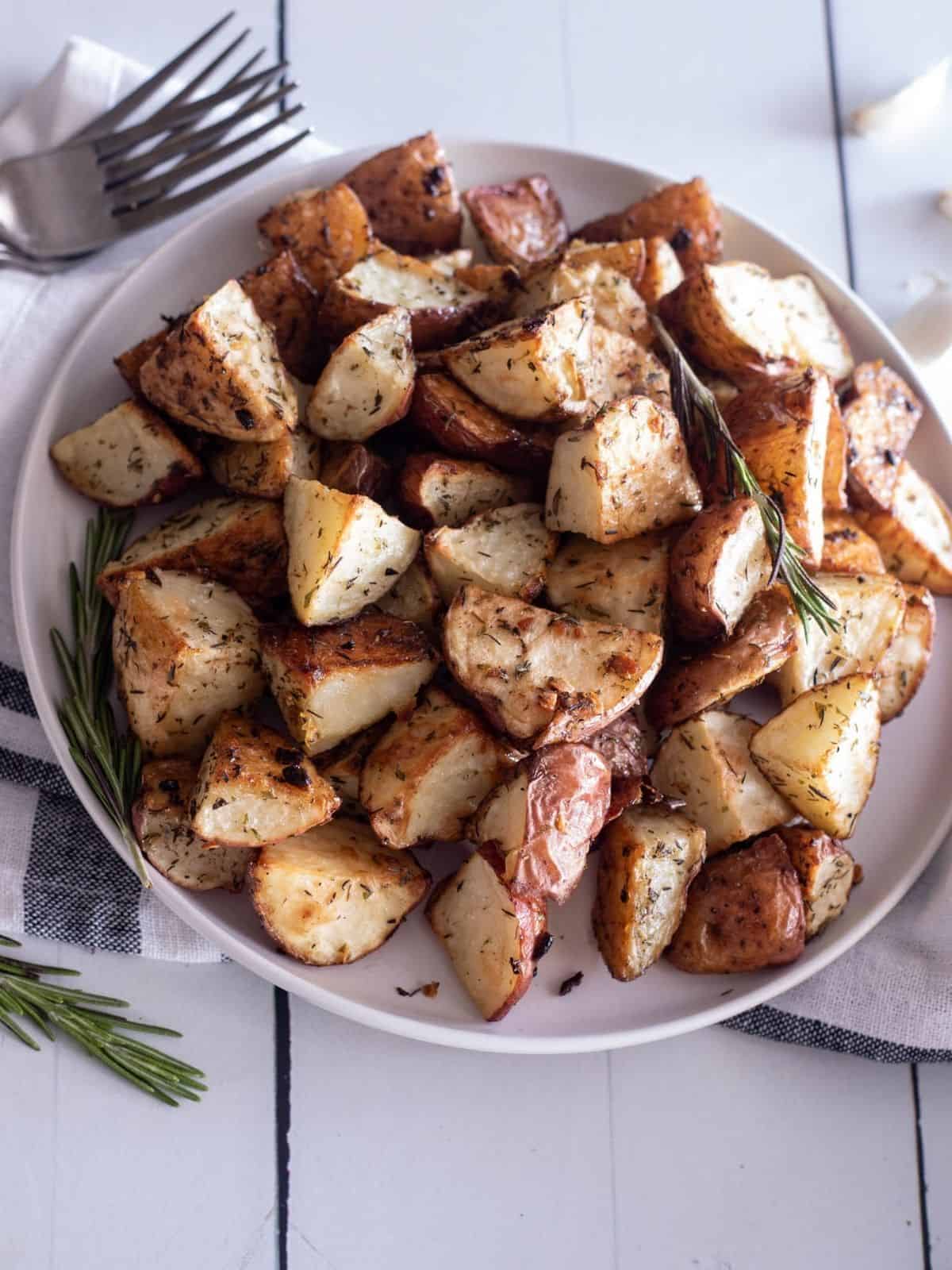 An overhead view of a round bowl filled with crispy roasted red potatoes topped with rosemary twigs. 