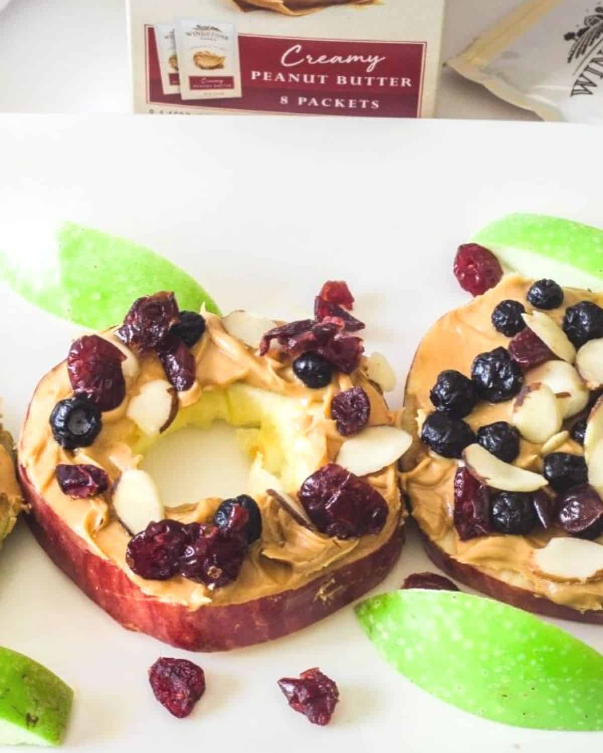 An apple slice topped with a layer of peanut butter, then dried fruit and sliced almonds.