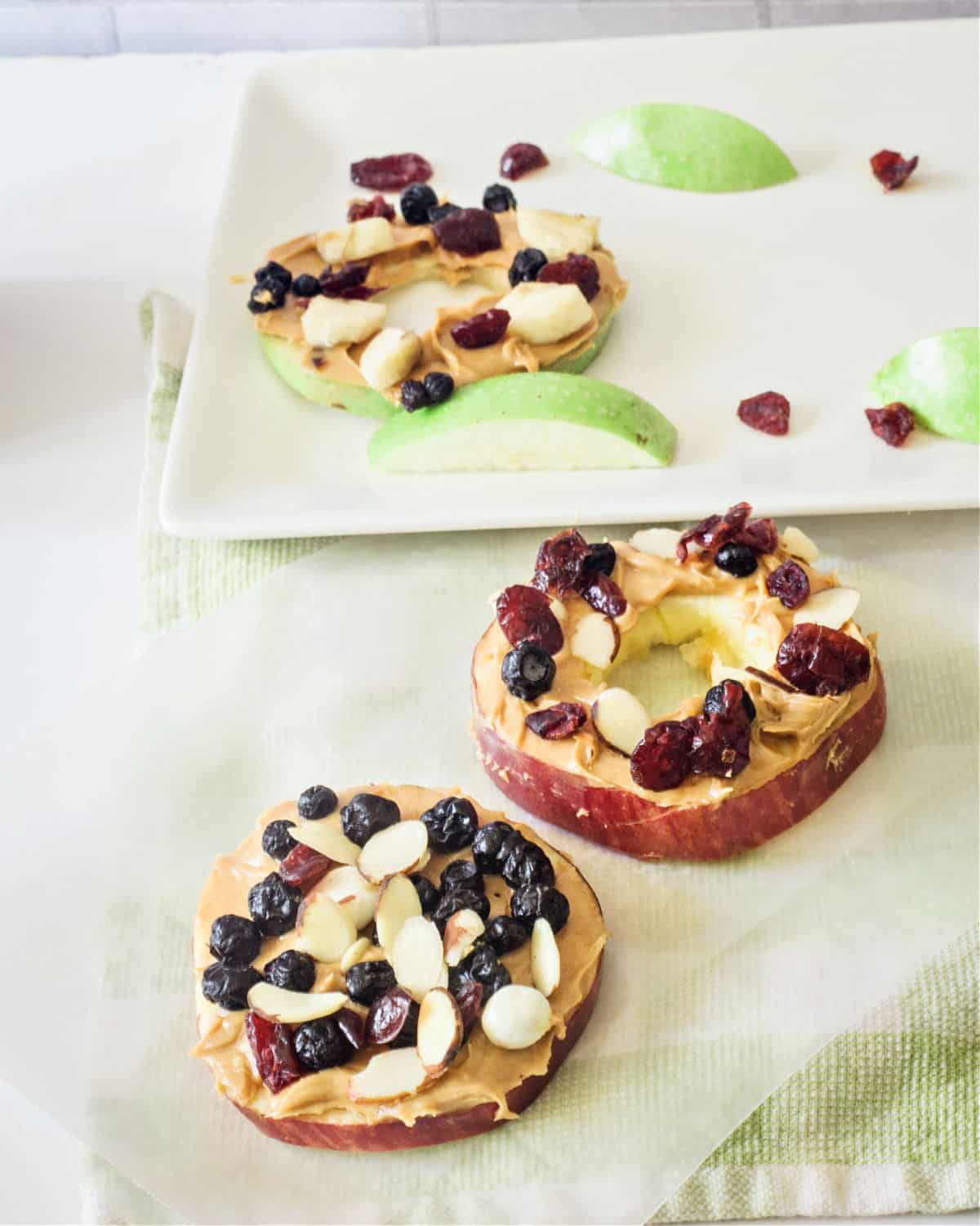 Sliced apples topped with peanut butter, raisins, blueberries, and dried fruit.