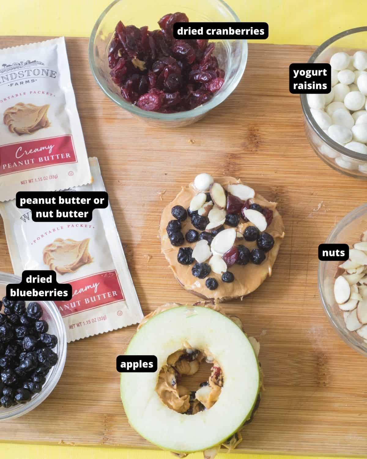 An array of ingredients of apple slices, peanut butter, dried fruit, nuts, raisins with text overlay.