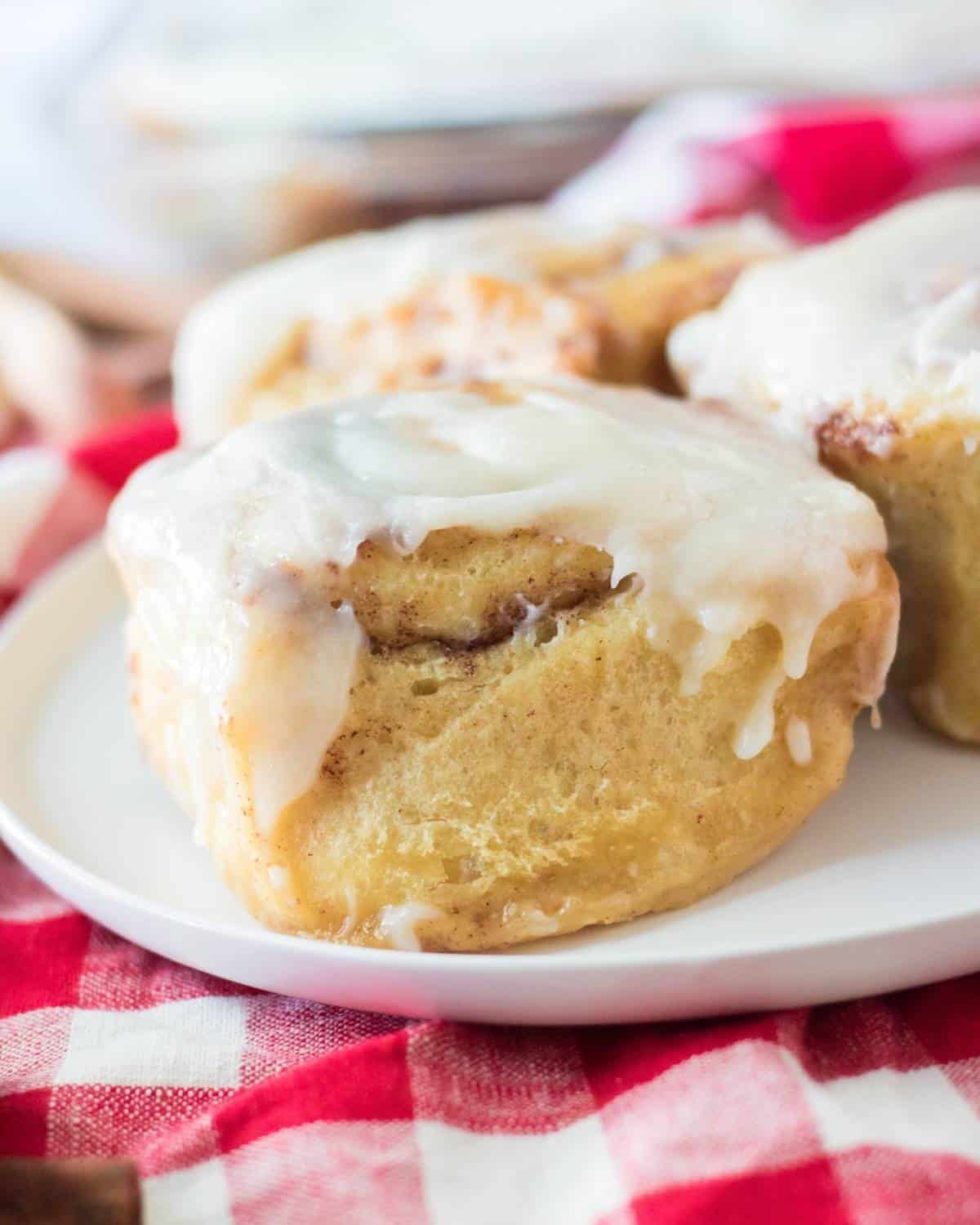 A baked cinnamon roll on a white plate topped with frosting.