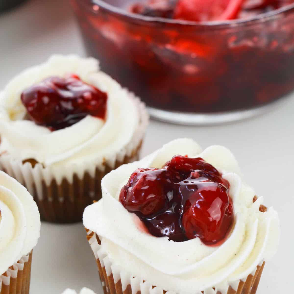 A vanilla cinnamon frosted cupcake with a dollop of cherry pie filling in the center. 