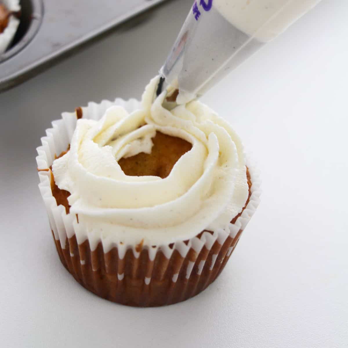 A cupcake being frosted with vanilla cinnamon frosting through a piping bag.