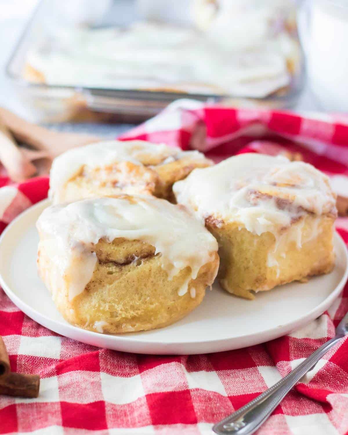 Tik tok recipe of cinnamon rolls topped with frosting on a white plate. 