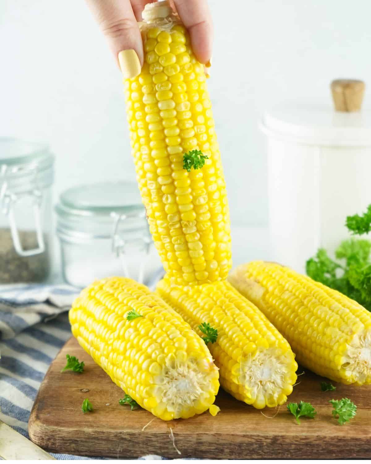 Three ears of corn on a cutting board and another ear of corn above them being held.