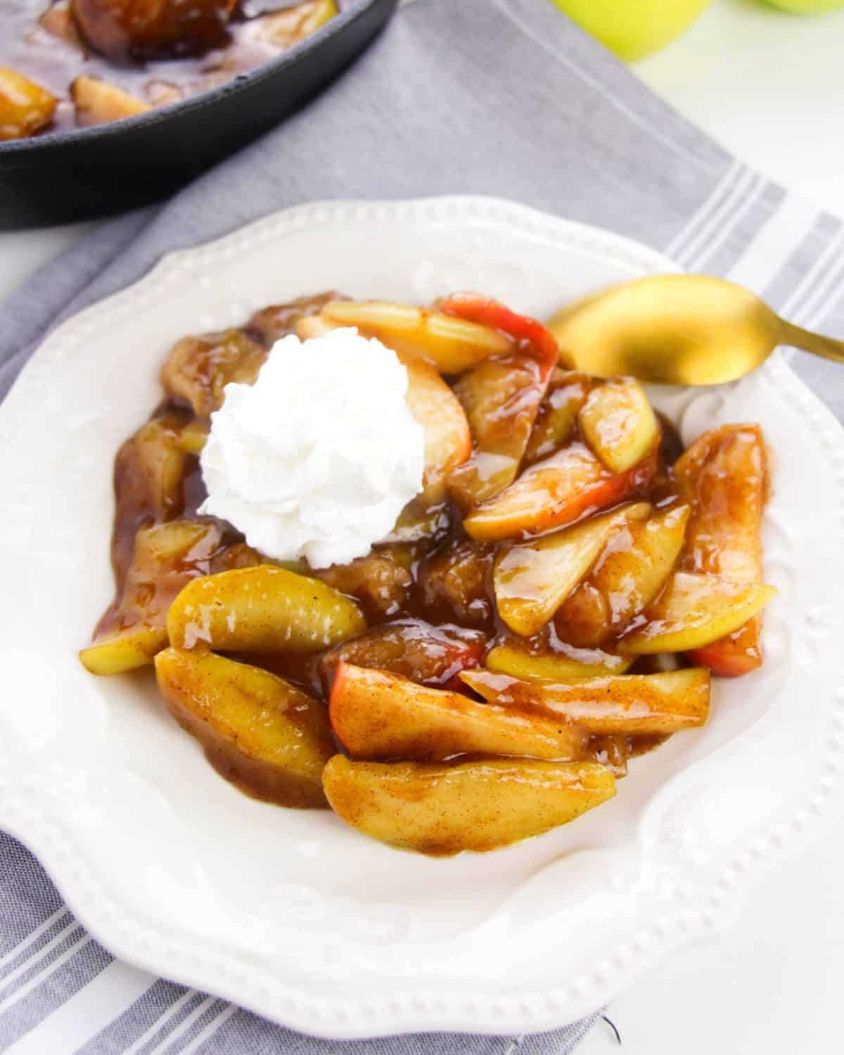 A white plate with fried apples topped with whipped cream. 