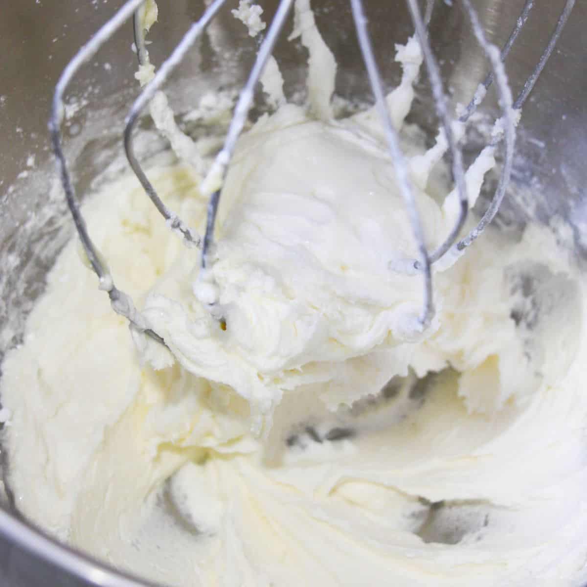 A large mixing bowl with a whisk attached and whipped cream being mixed in the bowl. 