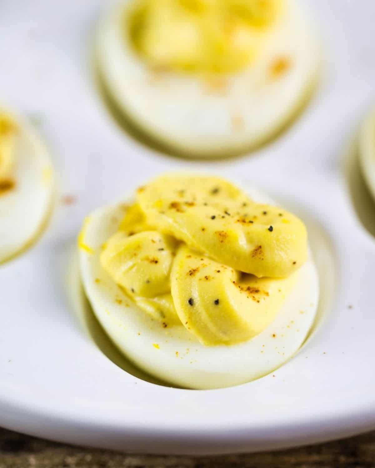 A deviled egg topped with a sprinkle of paprika and cracked black pepper on a white plate.